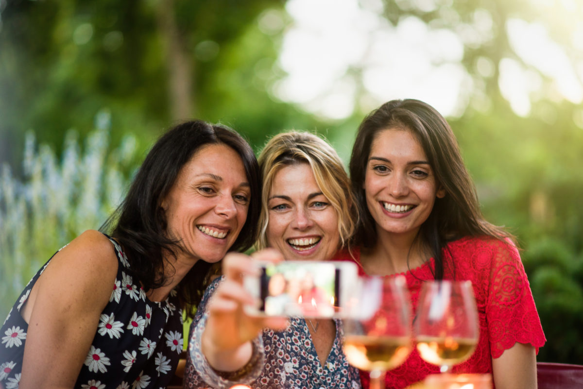 three woman taking a selfie while holding wine glasses