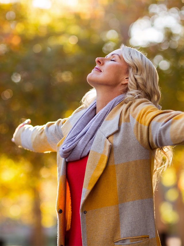 woman with outstretched arms facing the sun and smiling