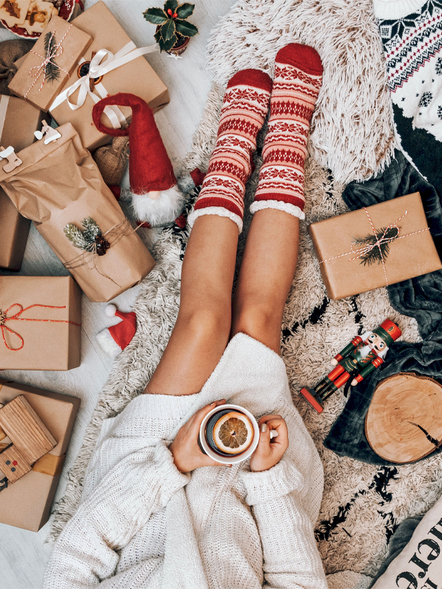 Woman relaxing on the ground holding a hot drink surrounded by Christmas presents