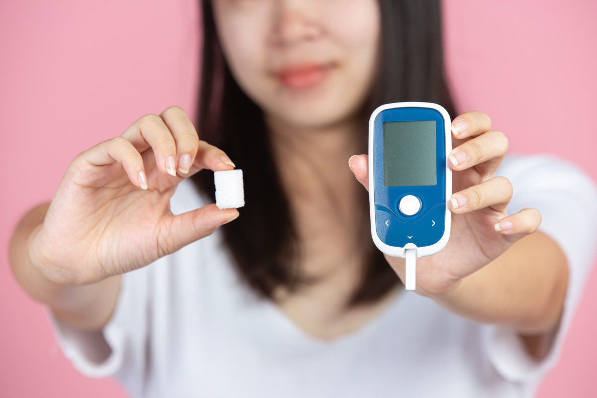 woman holding Glucose meter and sugar cubes on pink background