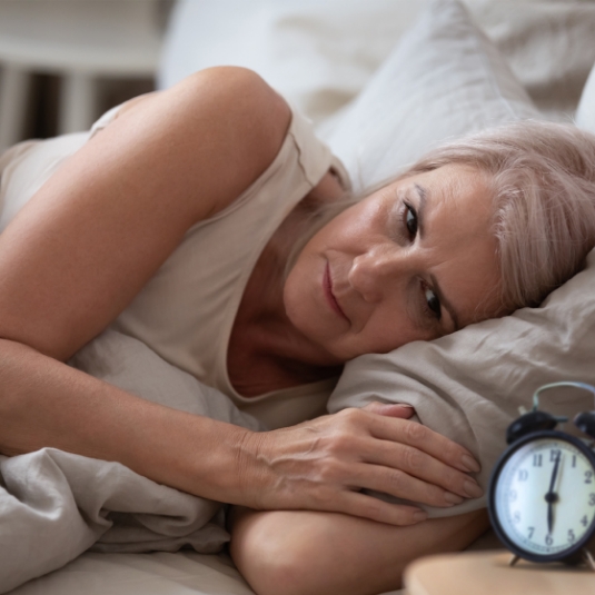 Woman in bed stares at clock struggling to sleep