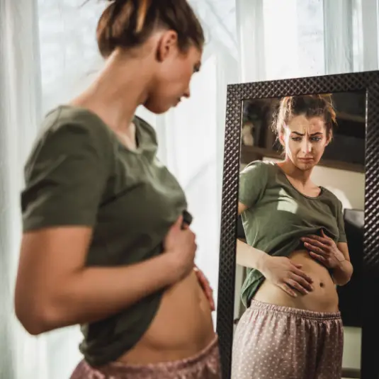 Woman looks in mirror with bloated stomach
